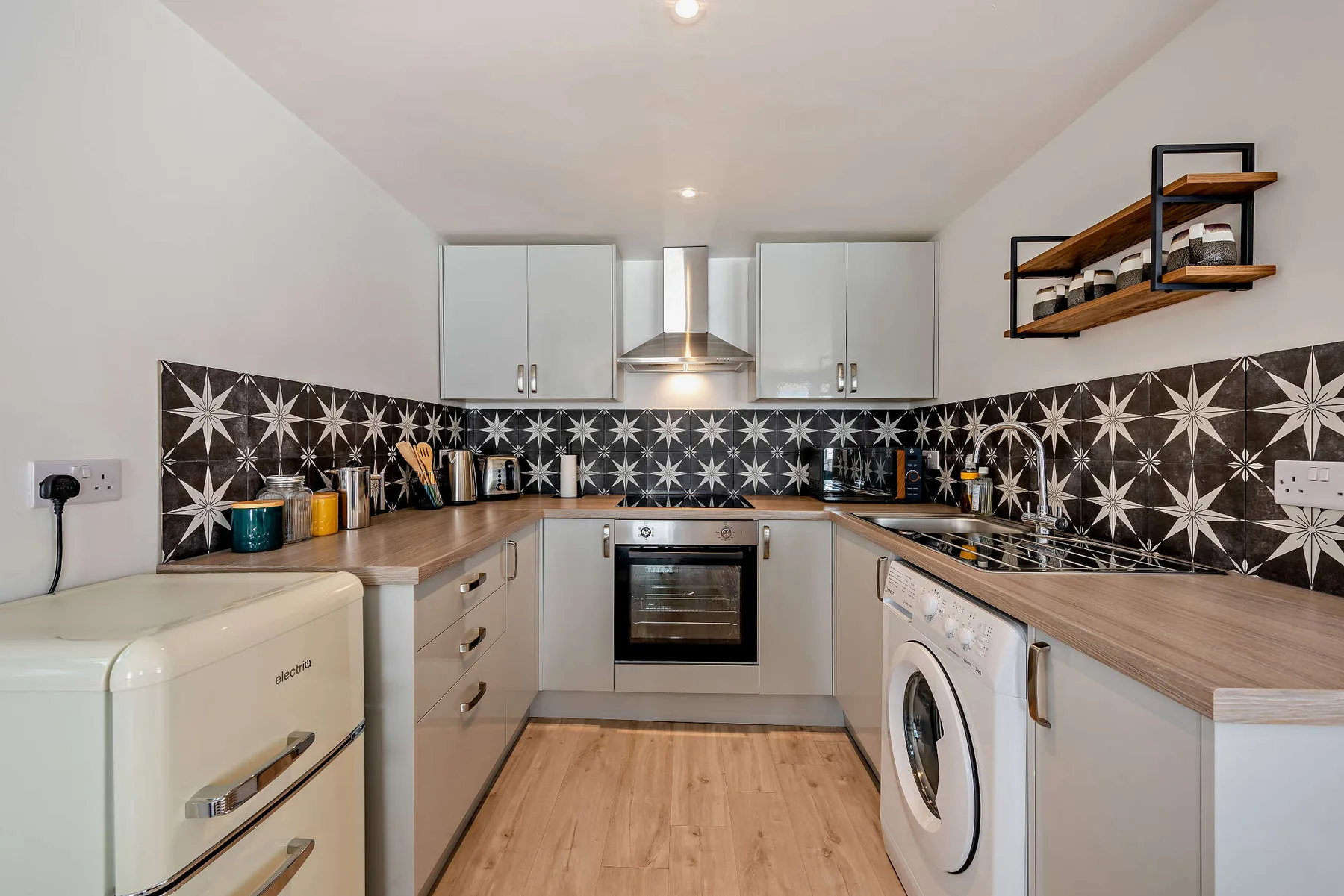 A compact kitchen with light cabinets, wood countertops, and a patterned backsplash.