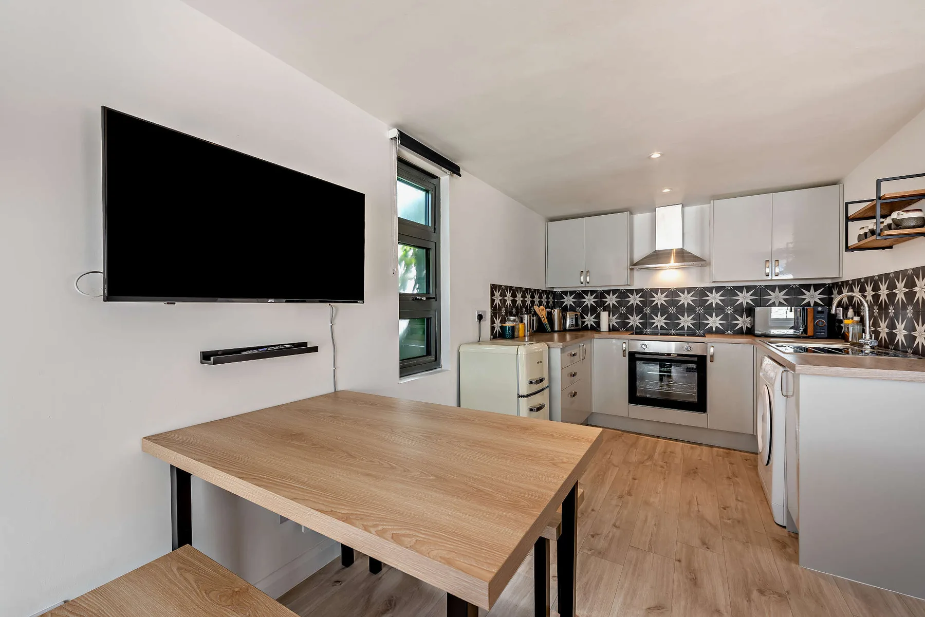 A modern kitchen with a wooden dining table and black-and-white patterned backsplash.
