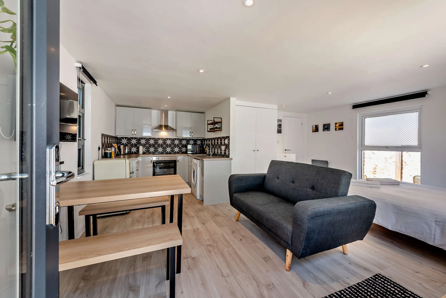 Open-plan studio room with a dark sofa, bed, and compact kitchen.