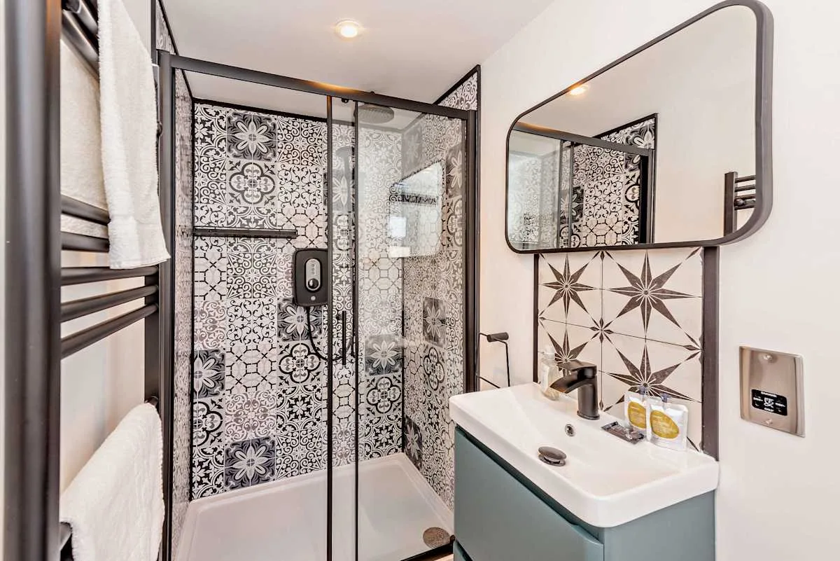 A bathroom with patterned tile, a glass shower, and a sink.