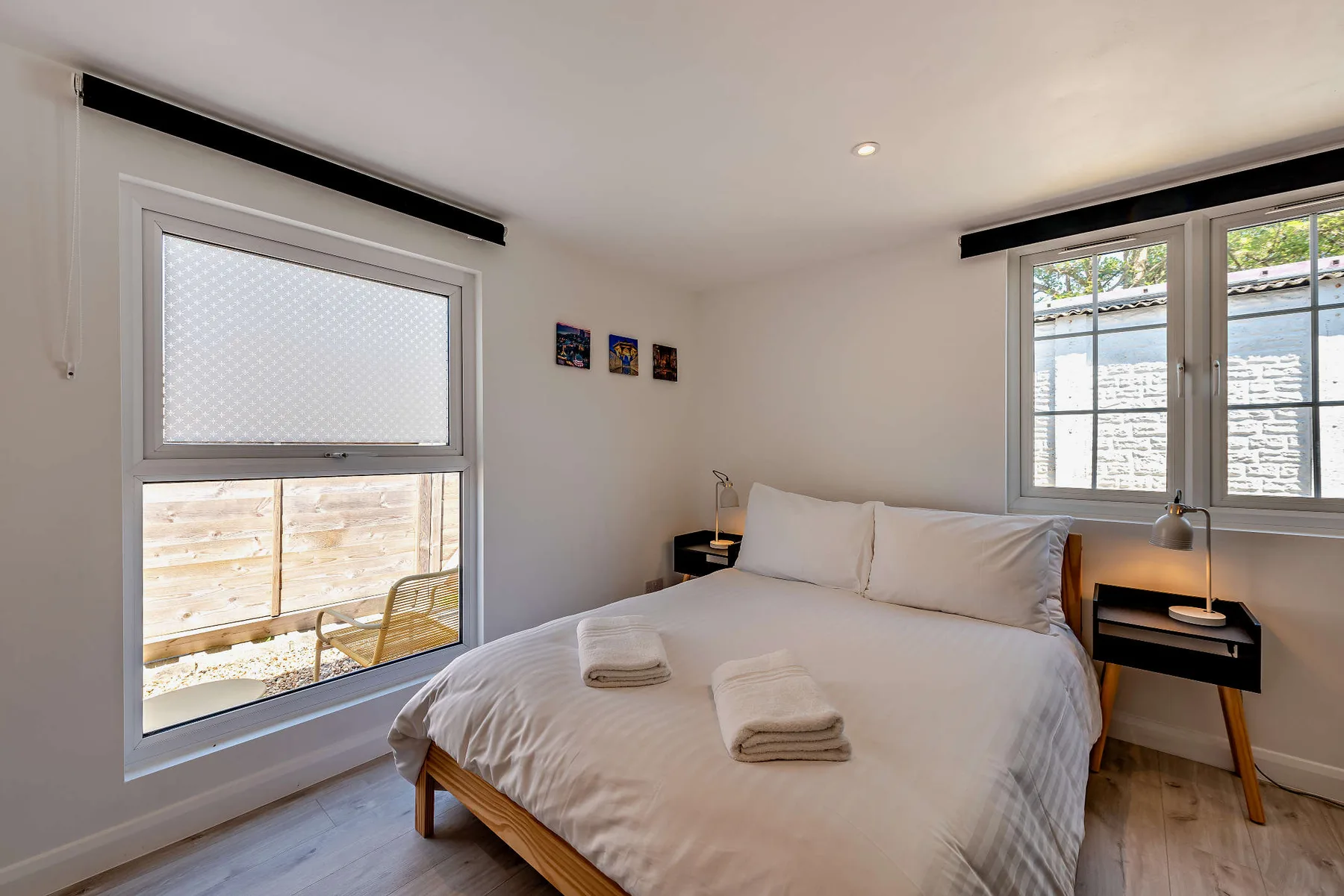 A bright bedroom with a bed, bedside tables, and windows.
