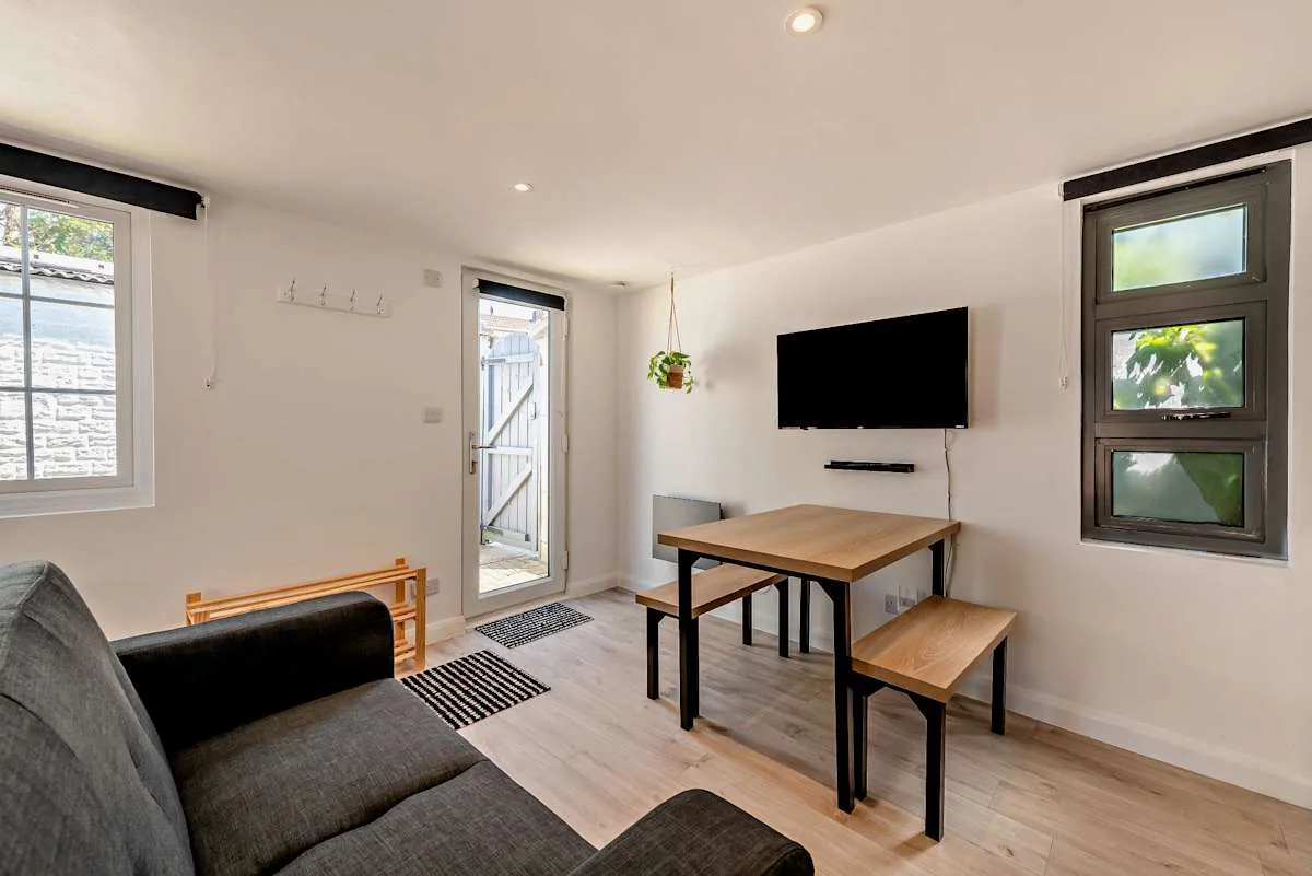 A bright living area with seating, a dining table, and a wall-mounted television.