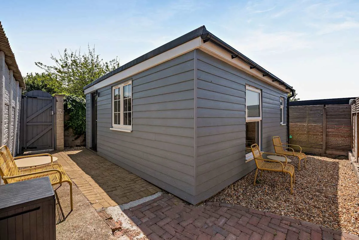 A small gray outbuilding stands beside a paved patio and gravel area.