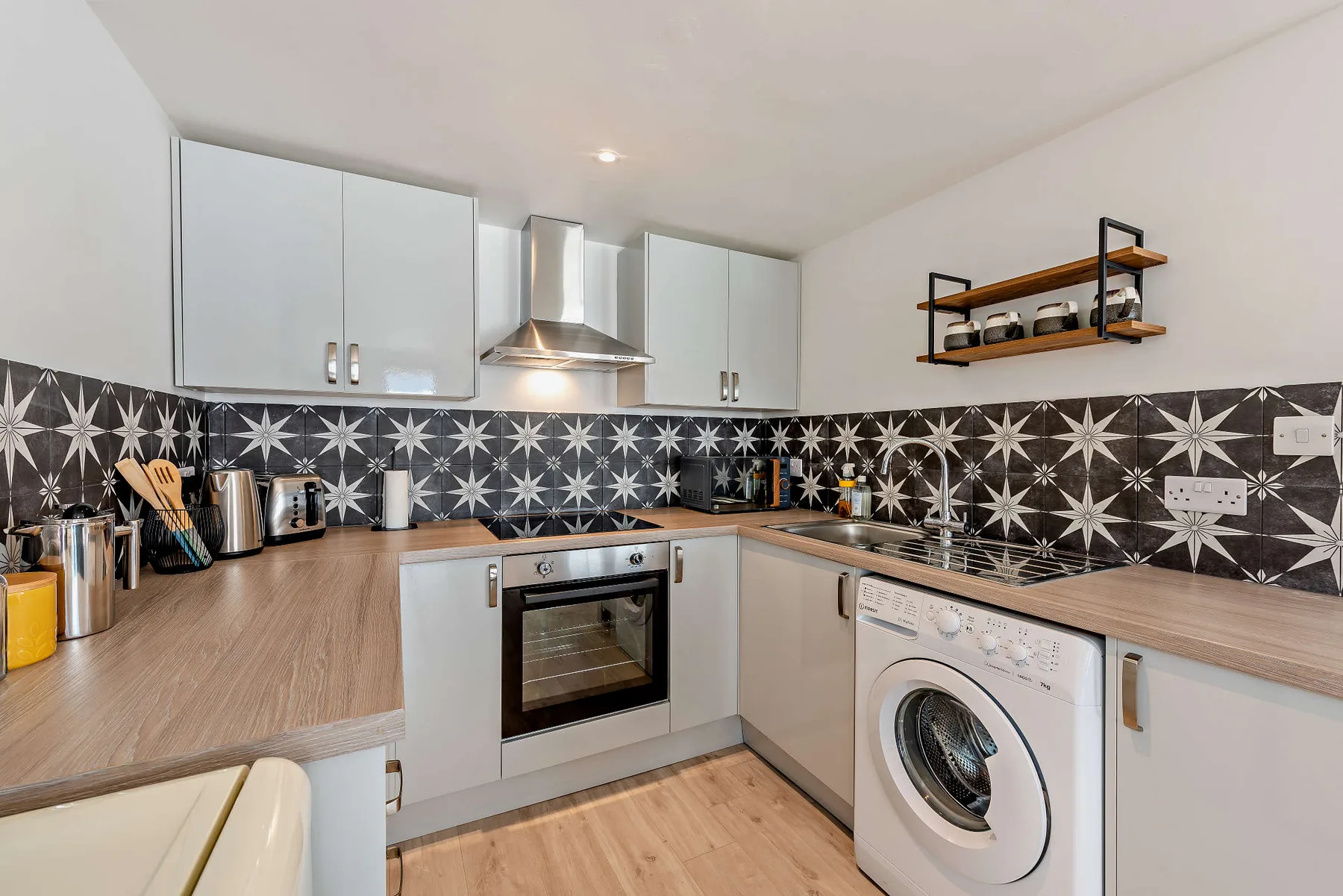 A modern kitchen with light cabinets, a patterned backsplash, and a washing machine.
