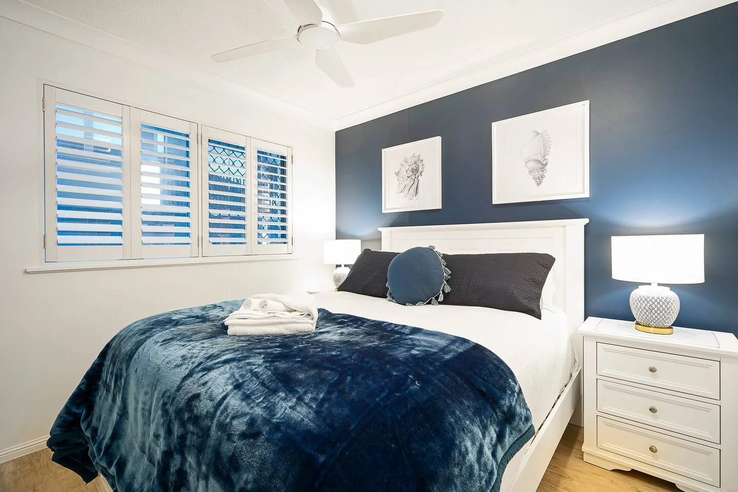 A bedroom with a bed covered by a dark blue blanket and framed artwork above it.