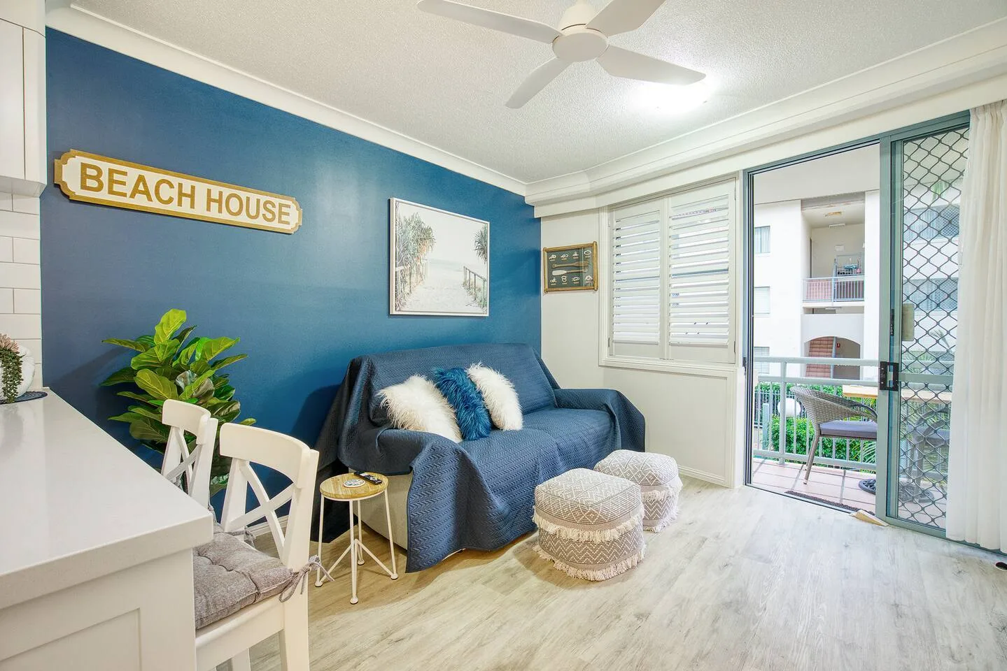 A bright living area with blue seating, a dining table, and an open balcony door.