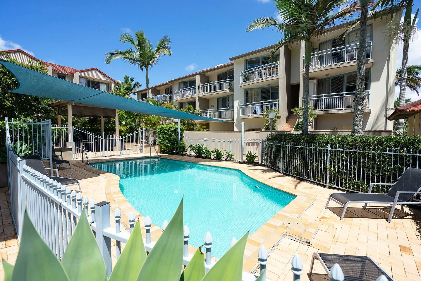 An outdoor swimming pool sits beside a multi-story building under a clear sky.
