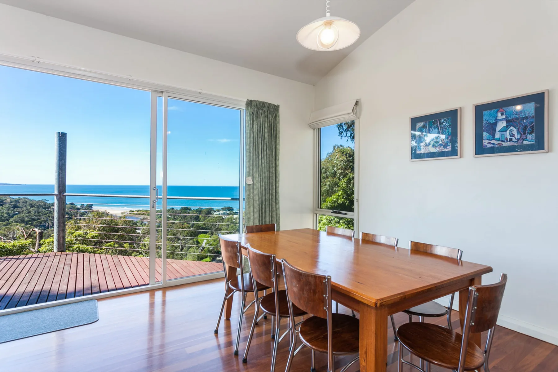 Un comedor con una mesa de madera junto a ventanas con vista al océano.