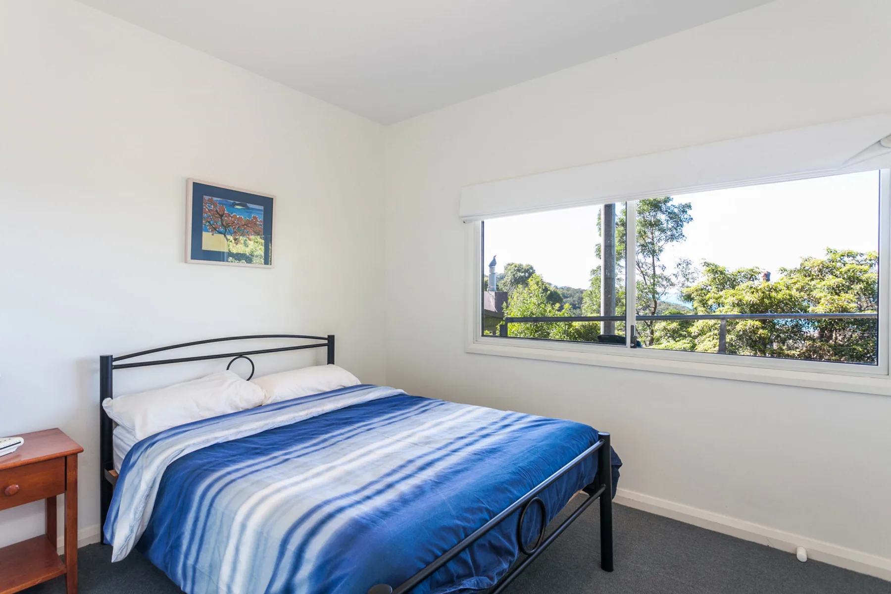 Dormitorio con ropa de cama azul y una ventana grande con vistas a árboles.