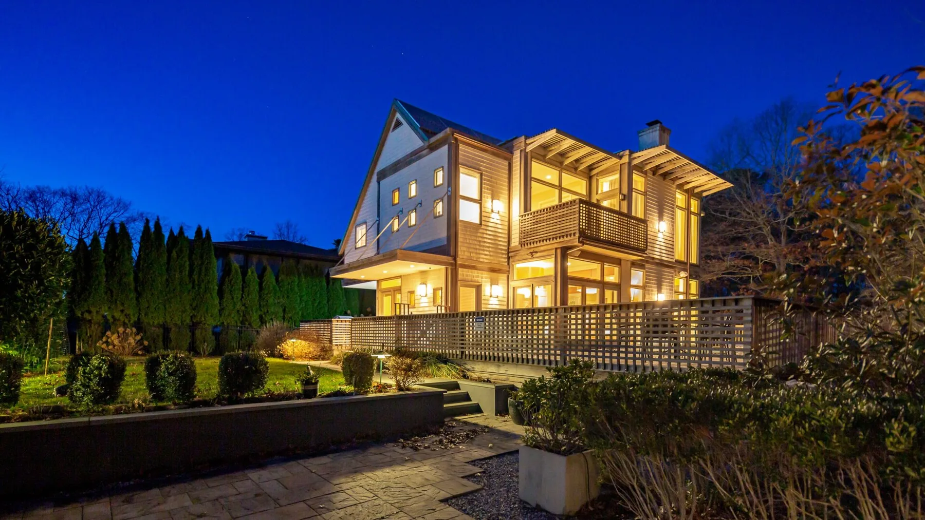 Una casa moderna resplandece con luces cálidas junto a jardines al anochecer.