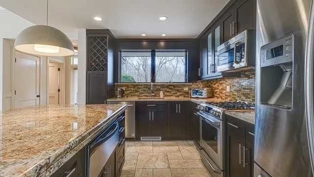 Una cocina moderna con gabinetes oscuros, encimeras de piedra y electrodomésticos de acero inoxidable.
