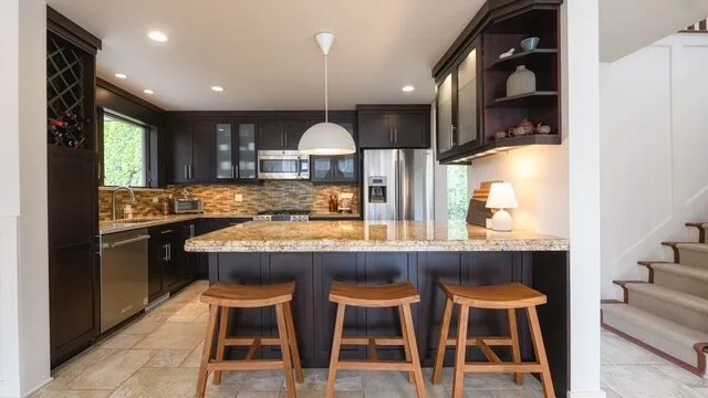 Una cocina con una isla central, taburetes de madera y gabinetes oscuros.