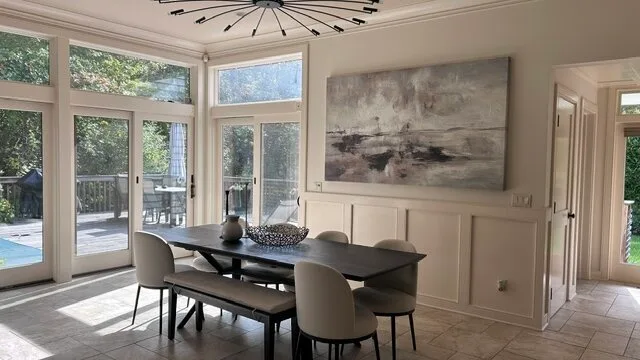 Un comedor luminoso con una mesa oscura junto a ventanas altas y puertas de vidrio.