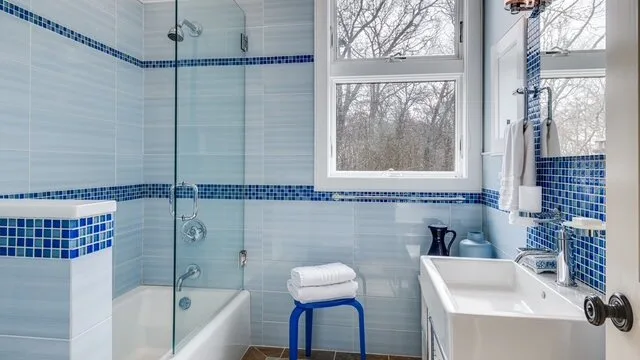 Un baño revestido de azulejos con bañera, ducha y lavabo bajo una ventana.