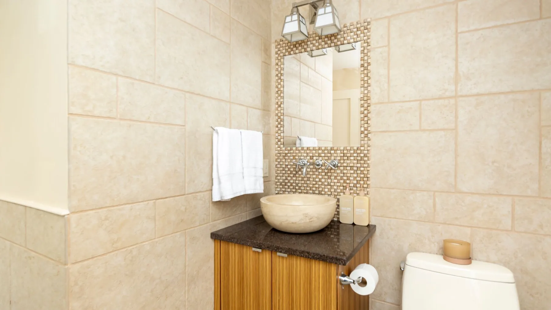 Un baño alicatado con una encimera oscura, lavabo sobrepuesto y espejo.