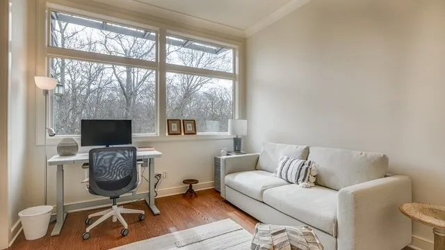 Una sala luminosa con un sofá blanco y un escritorio junto a ventanas grandes.