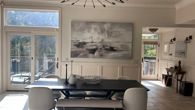Un comedor luminoso con una mesa junto a grandes puertas de vidrio y arte abstracto en la pared.