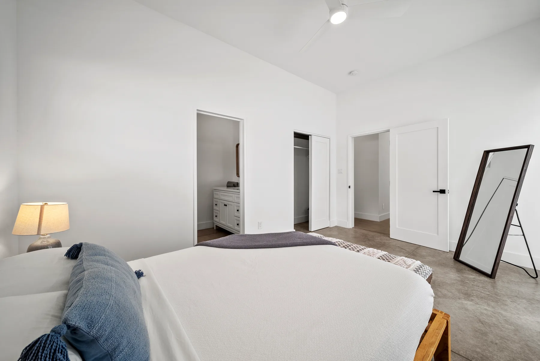 A bright bedroom with a bed, bedside lamp, and standing mirror.