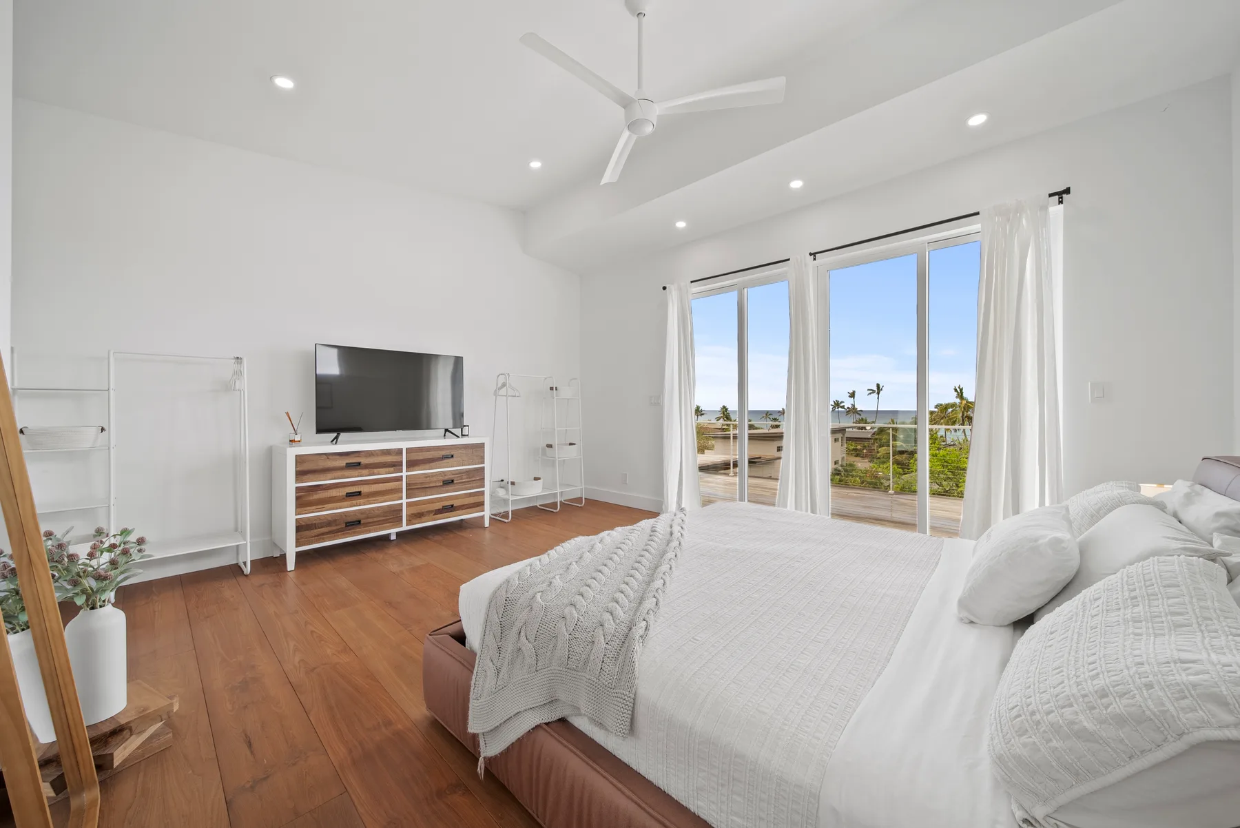 A bright bedroom with a large bed, television, and windows opening onto a balcony.