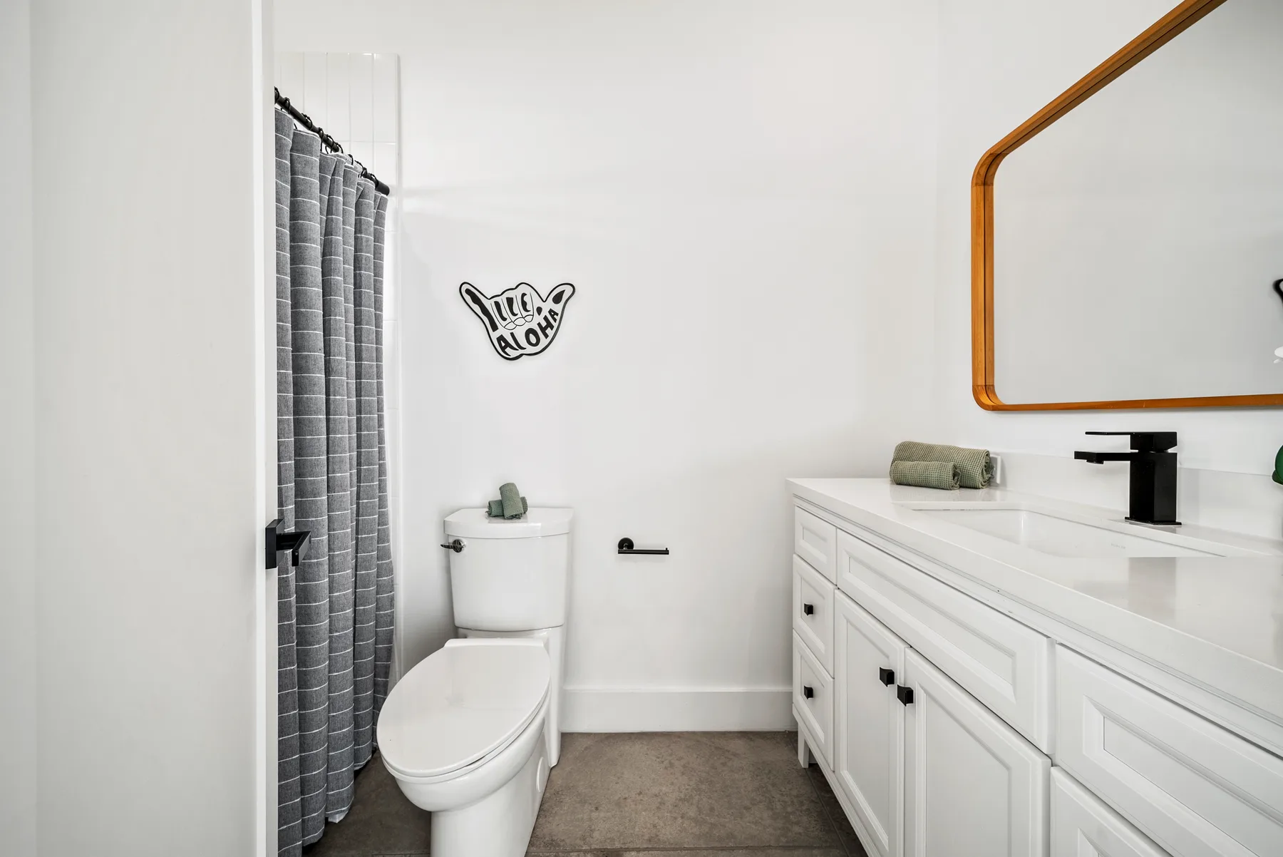 A bathroom with a toilet, shower curtain, and long vanity.
