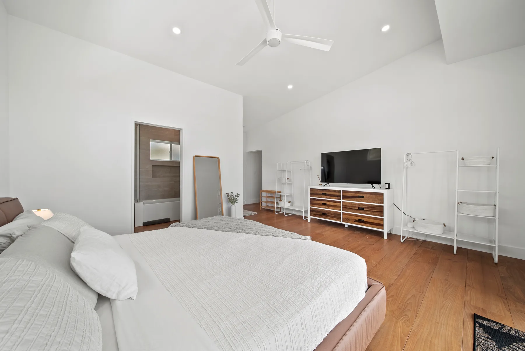 A bright bedroom with a large bed, television, and wooden floor.