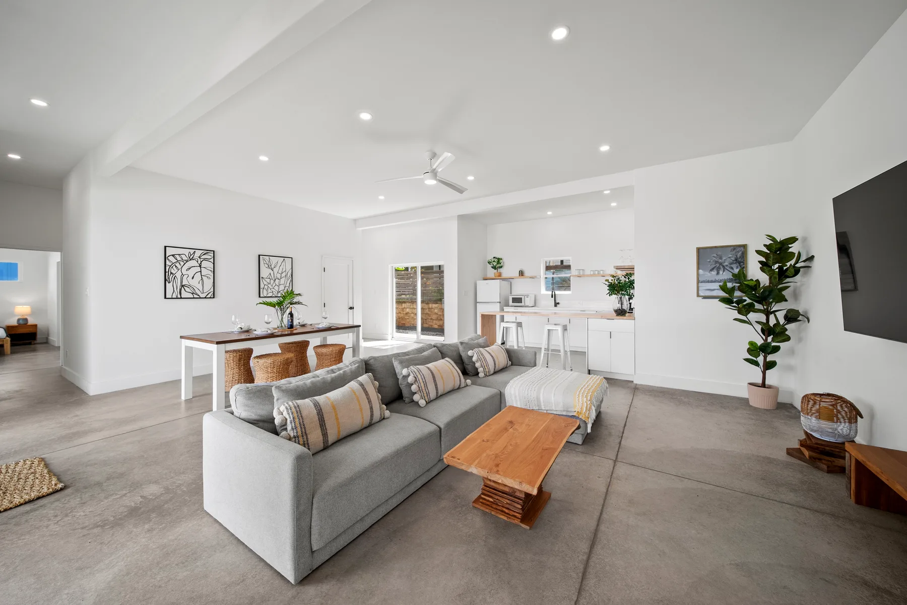 A bright living room with gray seating, a wooden coffee table, and a kitchen beyond.