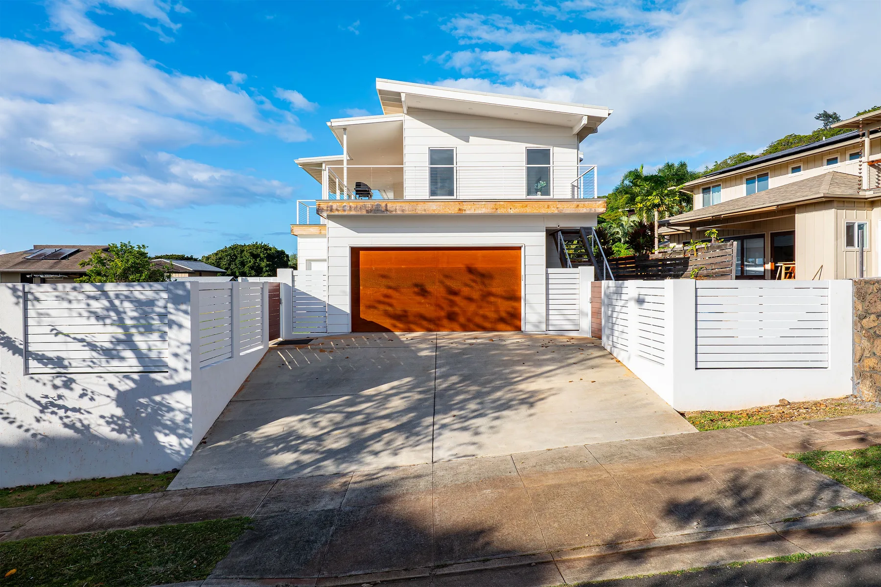A modern white house with an orange garage door and a sloped driveway.
