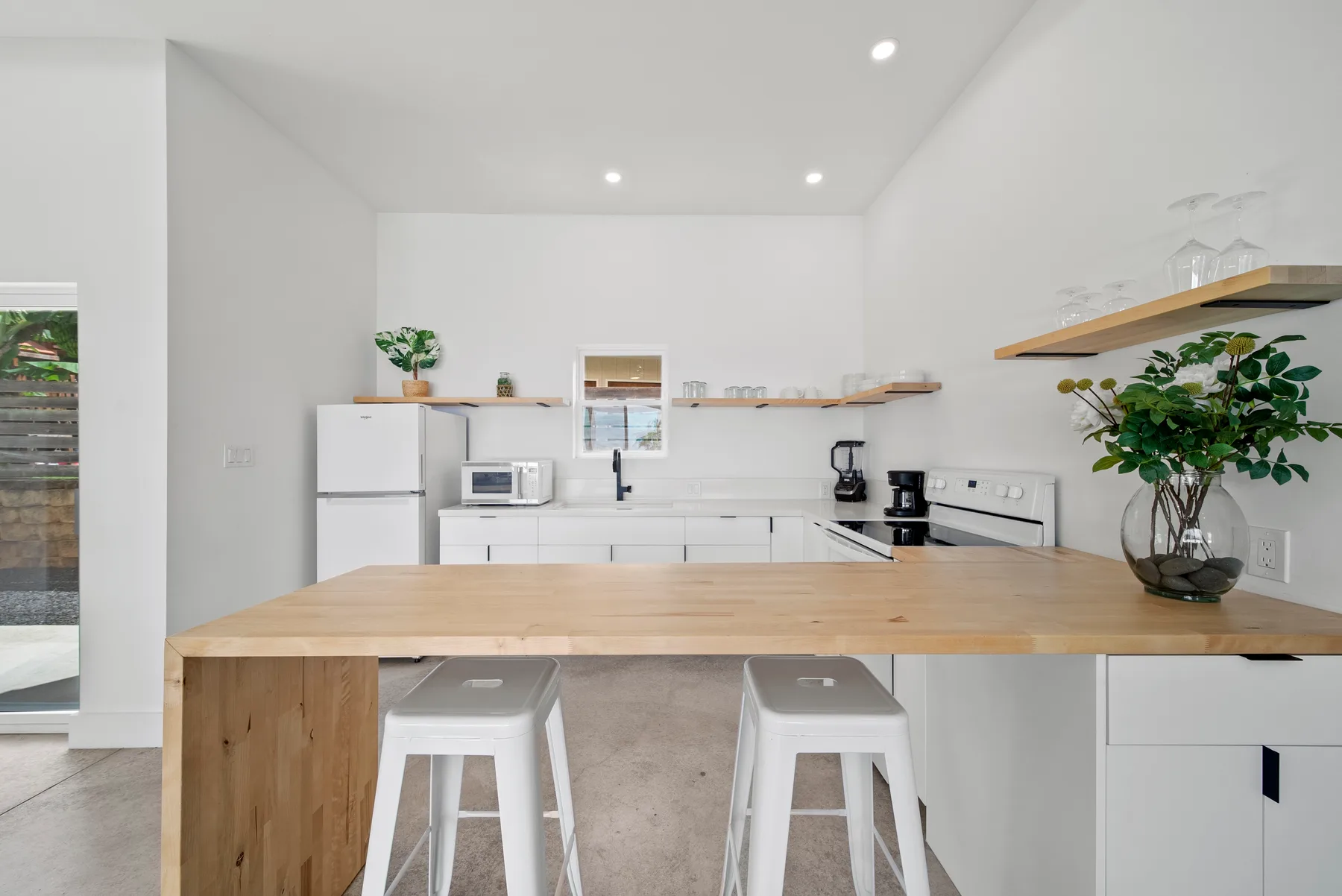 A bright white kitchen with a wooden island and two stools.