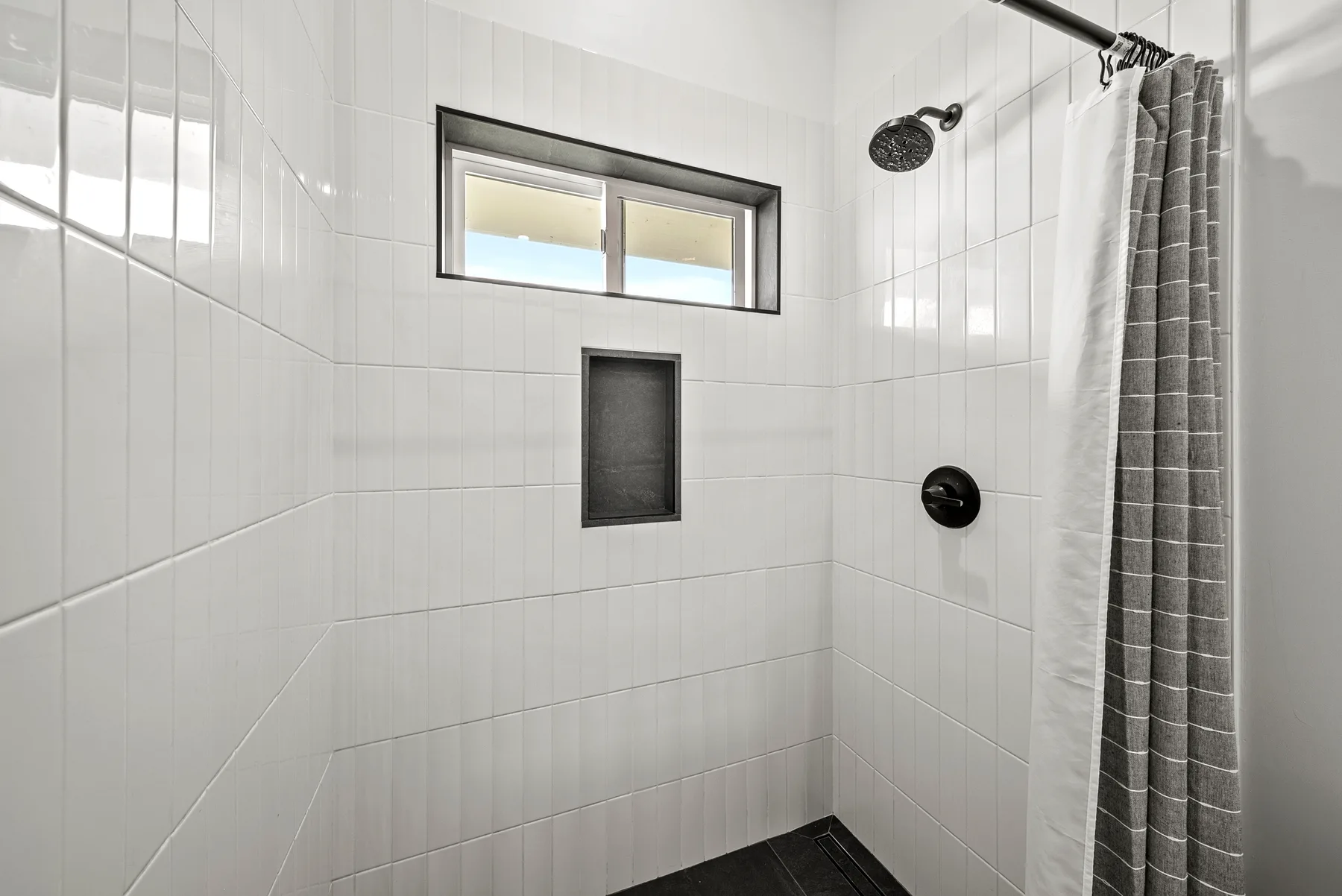 A tiled bathroom shower with a window and a curtain.