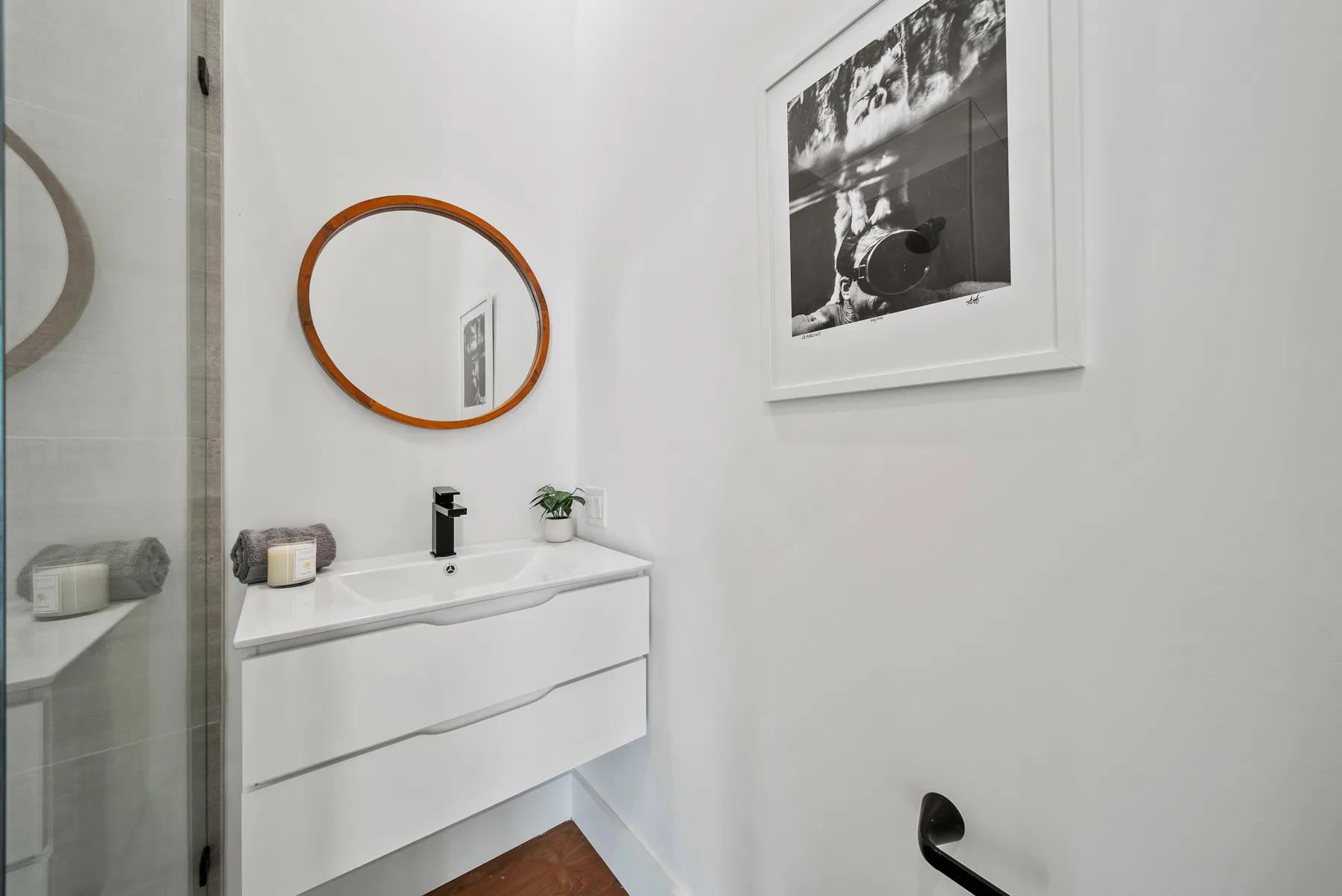 A bright bathroom with a white vanity, round mirror, and framed wall art.