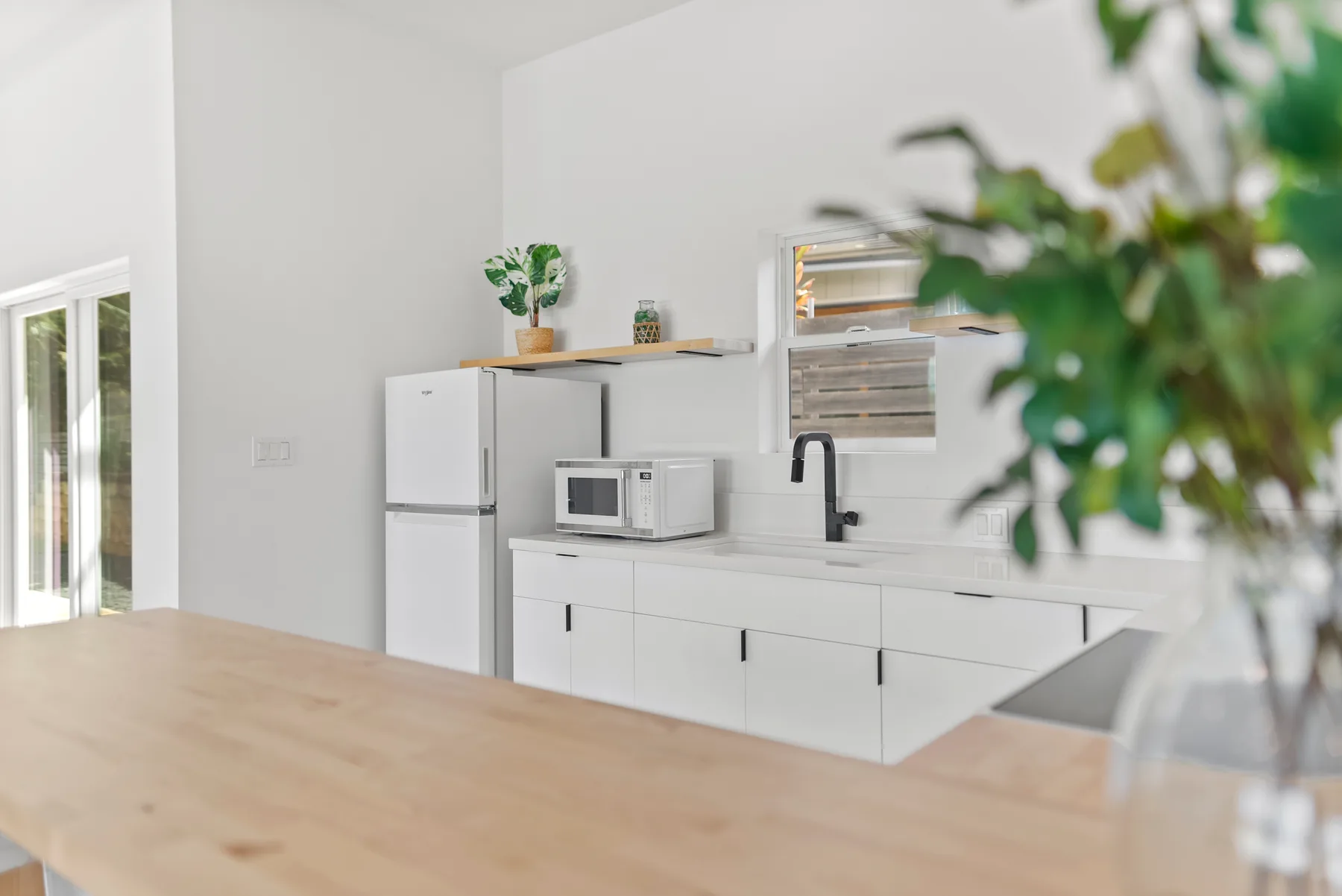 A bright kitchen with white cabinets, a refrigerator, and a countertop microwave.