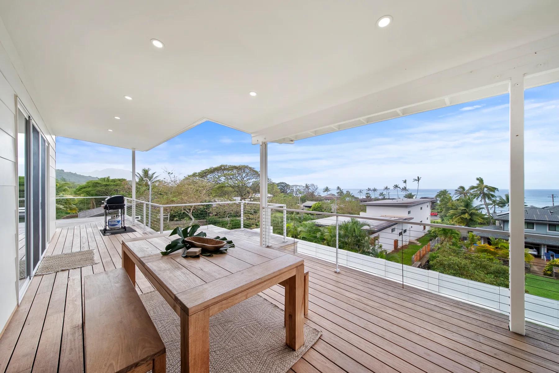 Una terraza exterior cubierta con una mesa de madera mira hacia la vegetación y el océano.
