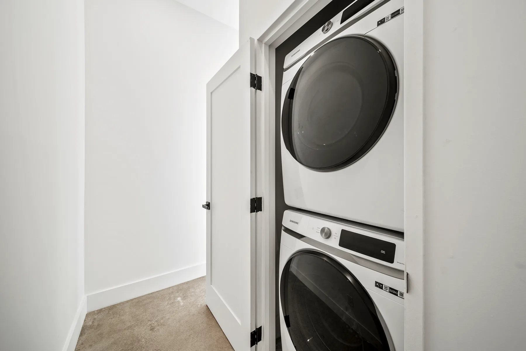 A laundry area with a stacked washer and dryer behind an open closet door.
