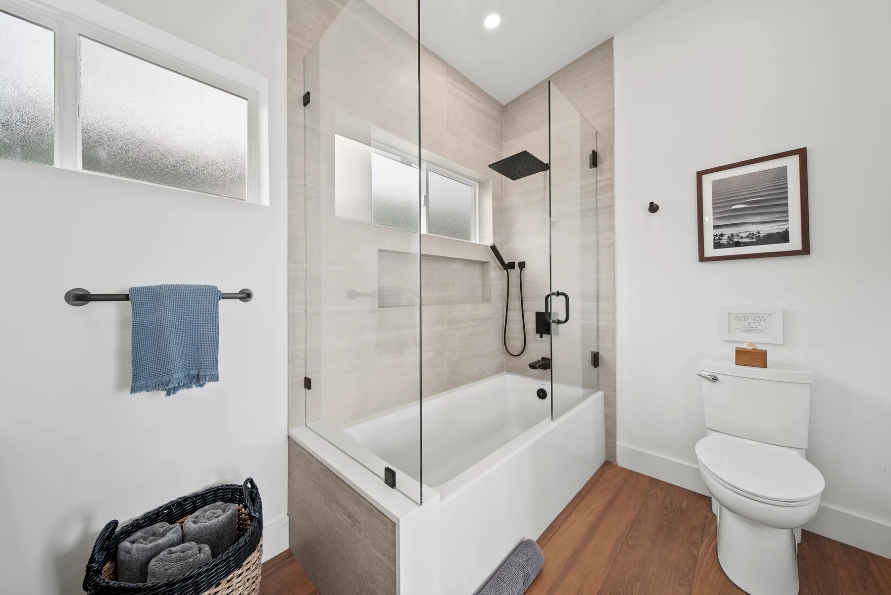 A bright bathroom with a bathtub, glass shower screen, and toilet.
