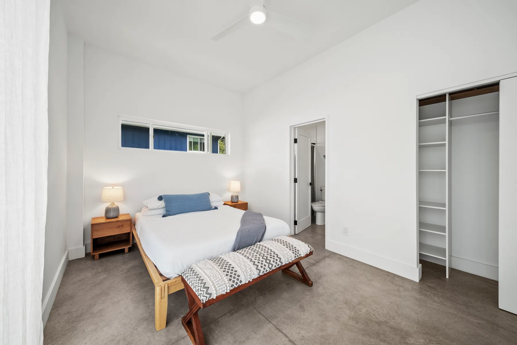 A bright bedroom with a bed, bedside tables, and an open closet.
