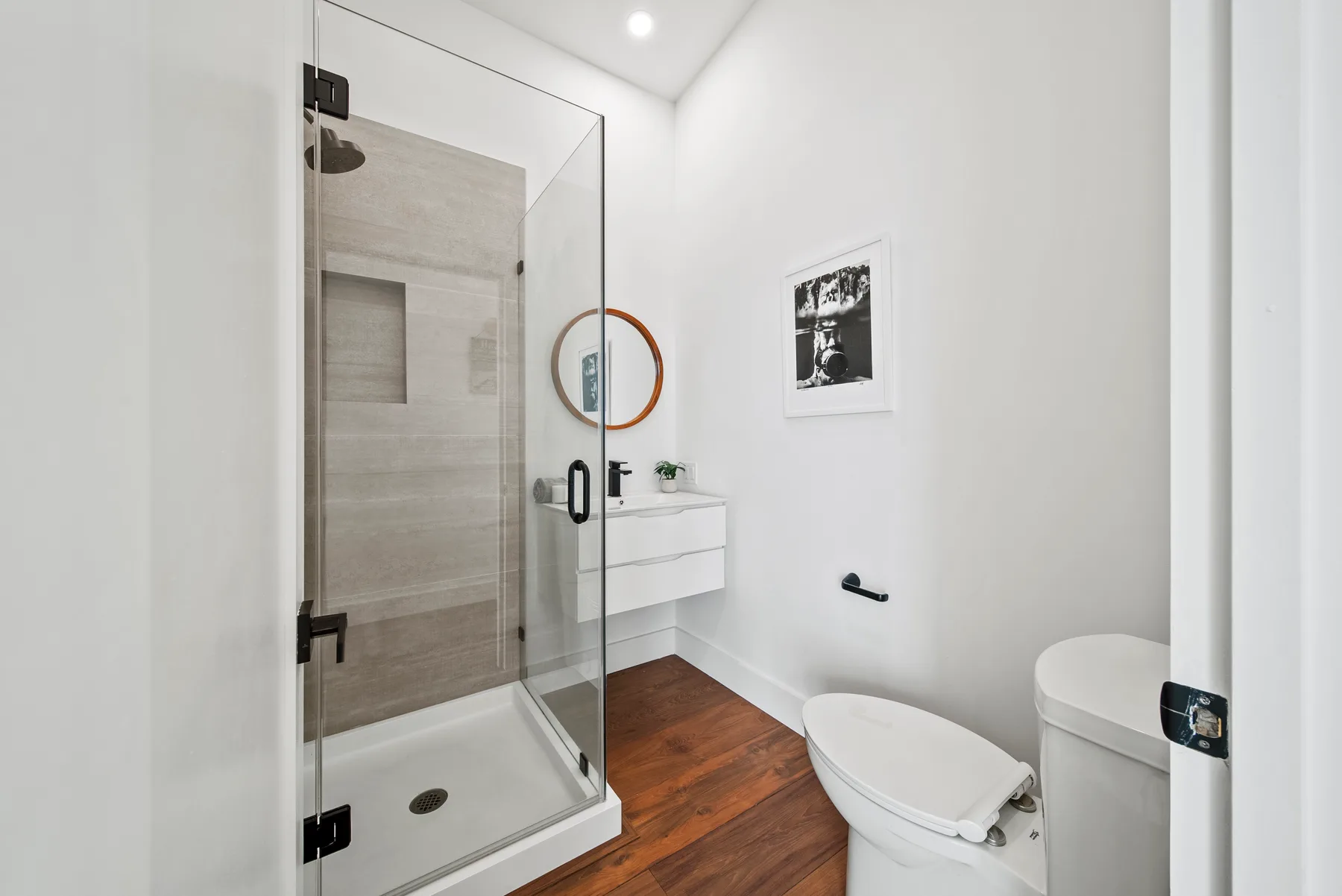 A bright bathroom with a glass shower, toilet, and wood-look flooring.