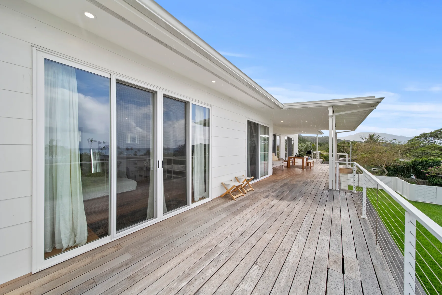 A wooden deck runs alongside a modern white house, with sliding glass doors.