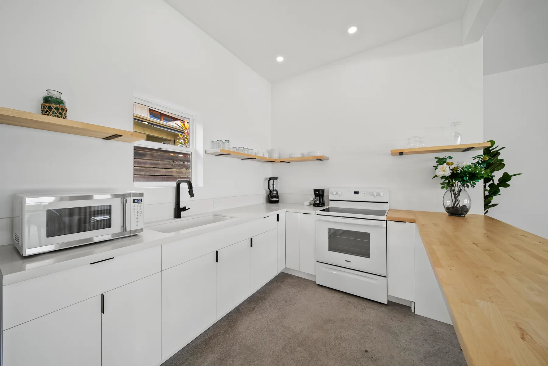 A bright white kitchen with a long wooden counter and built-in appliances.