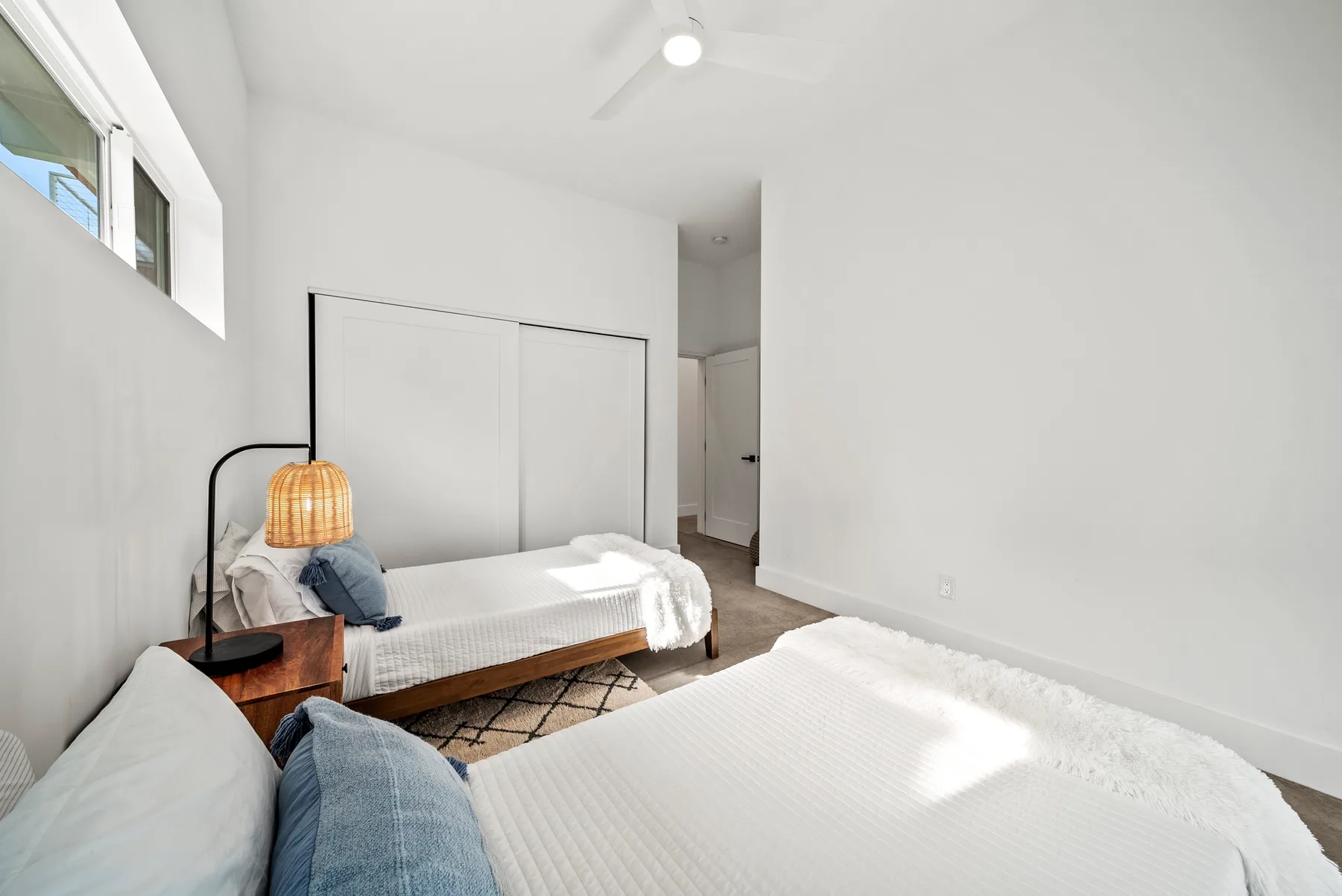 A bright bedroom with white bedding, a wooden bedside table, and a window.