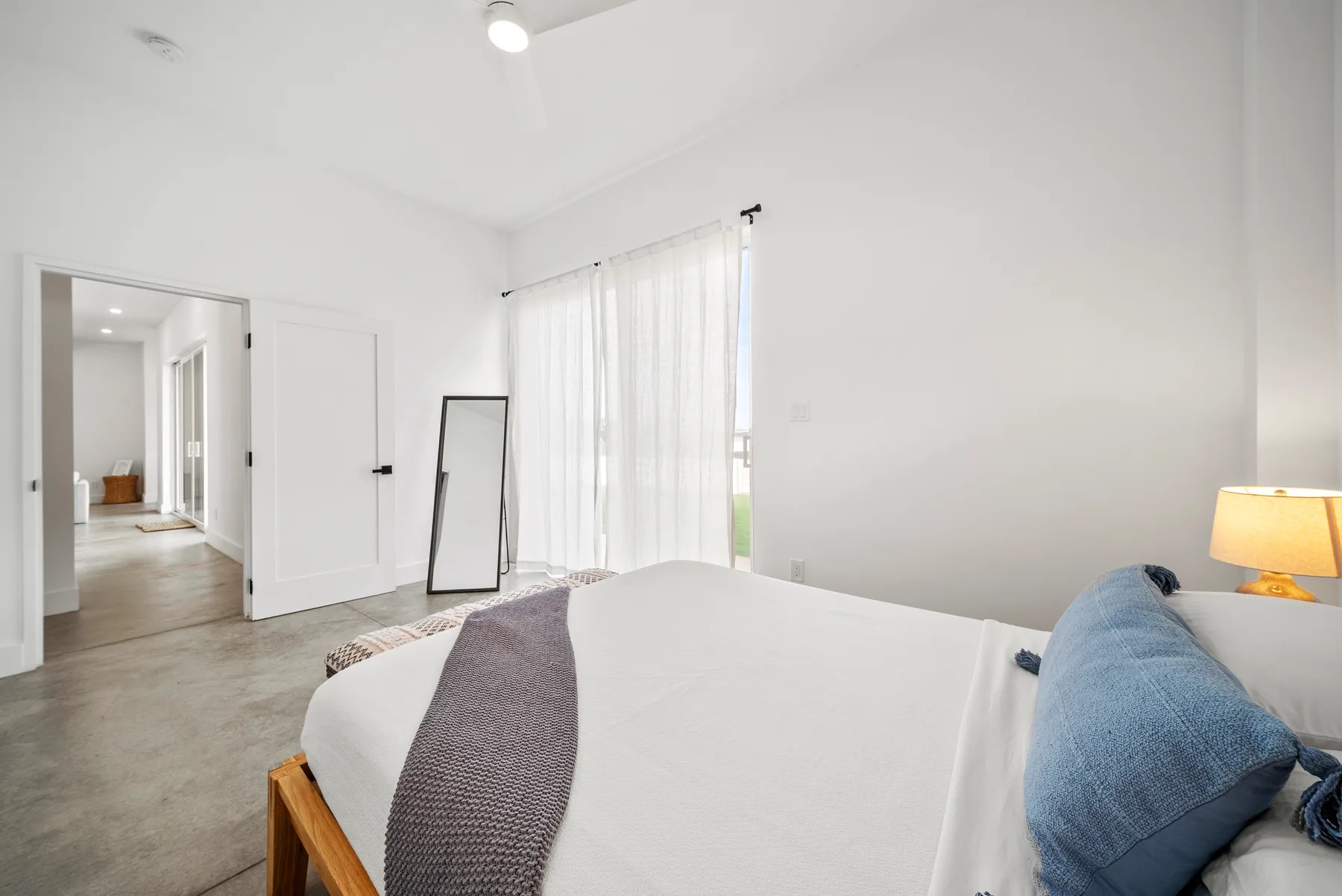 A bright bedroom with a neatly made bed beside a curtained window.