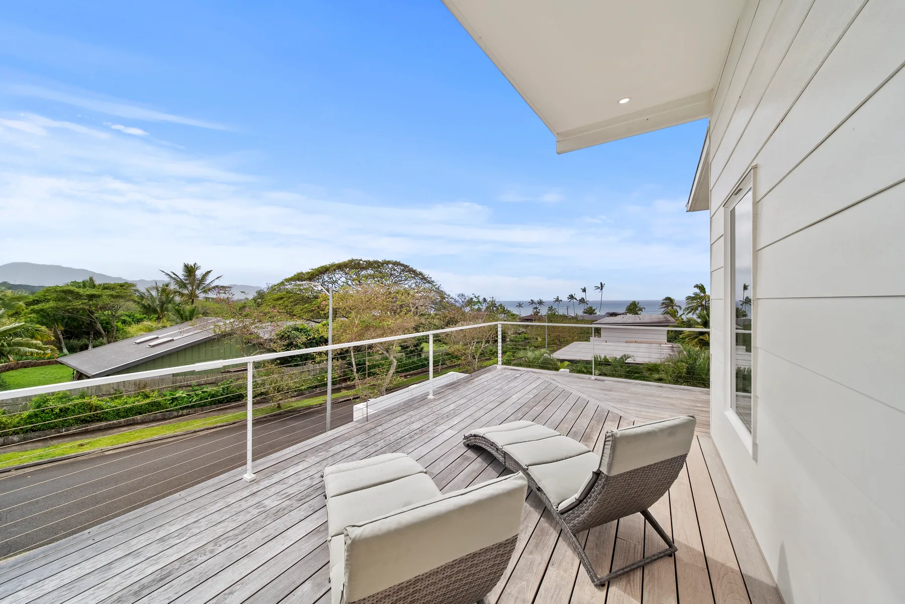 A wooden deck beside a house overlooks greenery and a distant stretch of water.