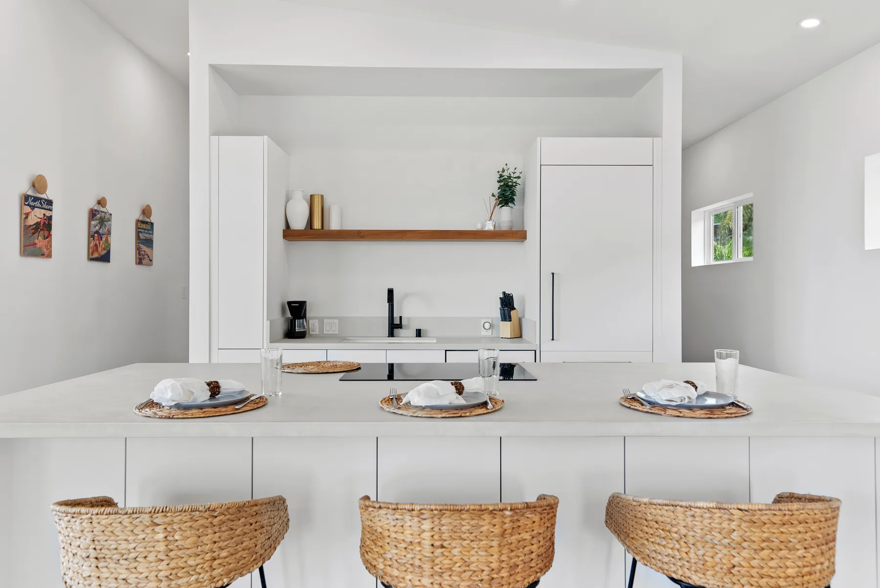A bright white kitchen with a long island and woven seating.