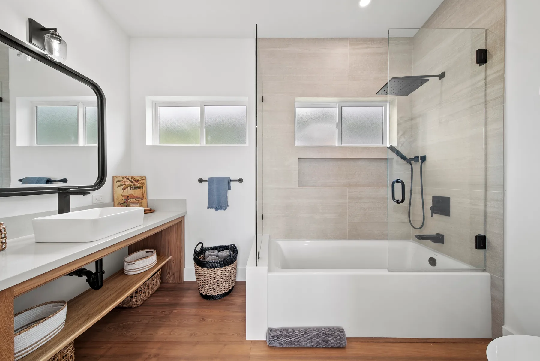 A bright bathroom features a vanity beside a bathtub with a glass shower screen.