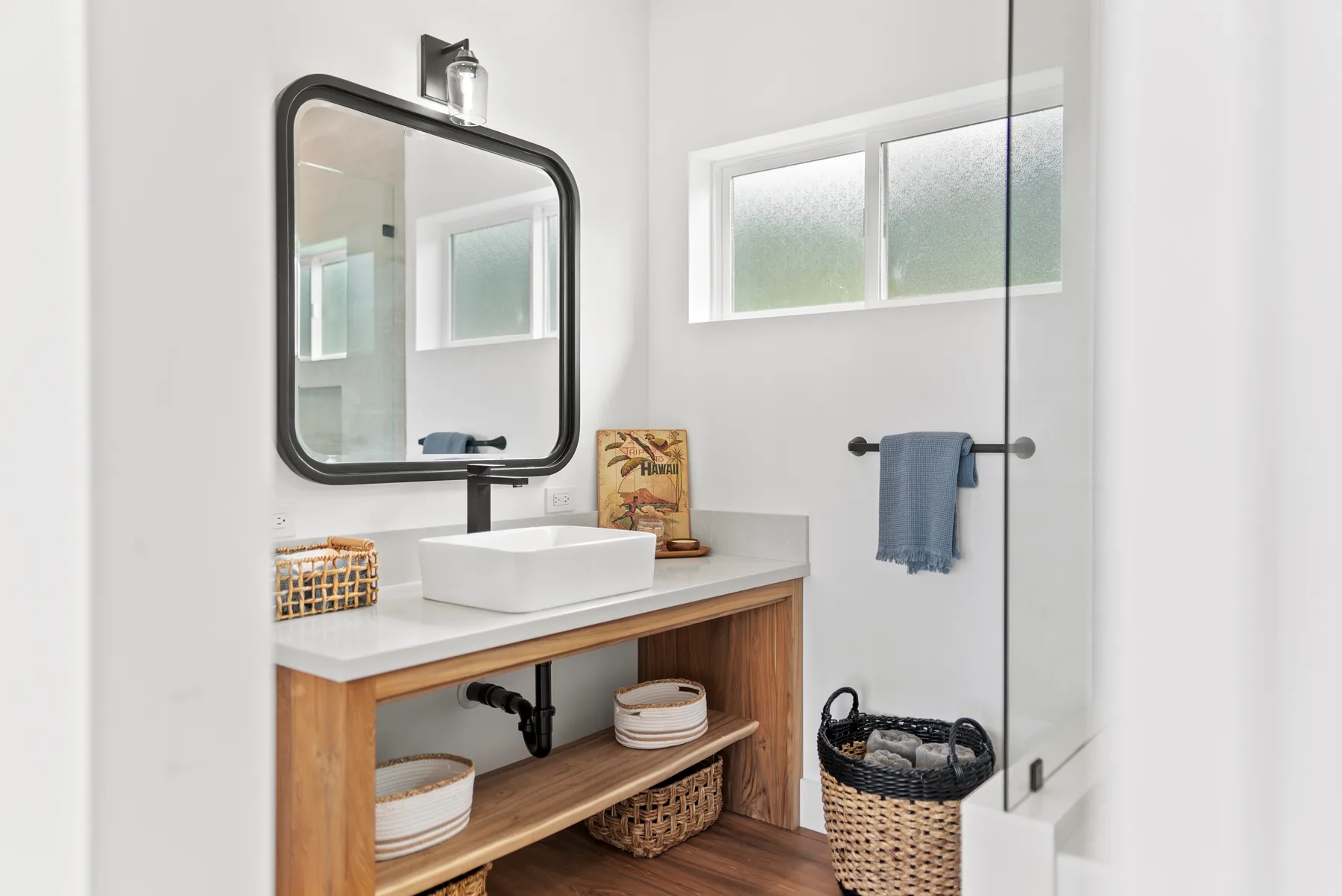 A bright bathroom with a wood vanity, vessel sink, and glass shower.