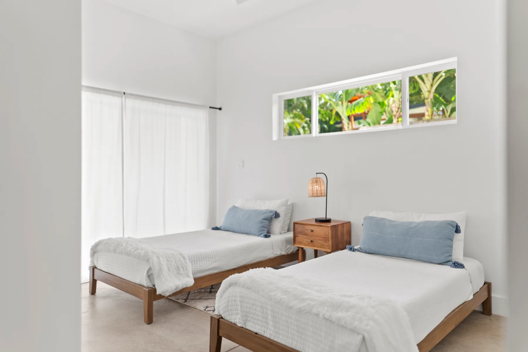 A bright bedroom with two beds and a narrow window overlooking greenery.