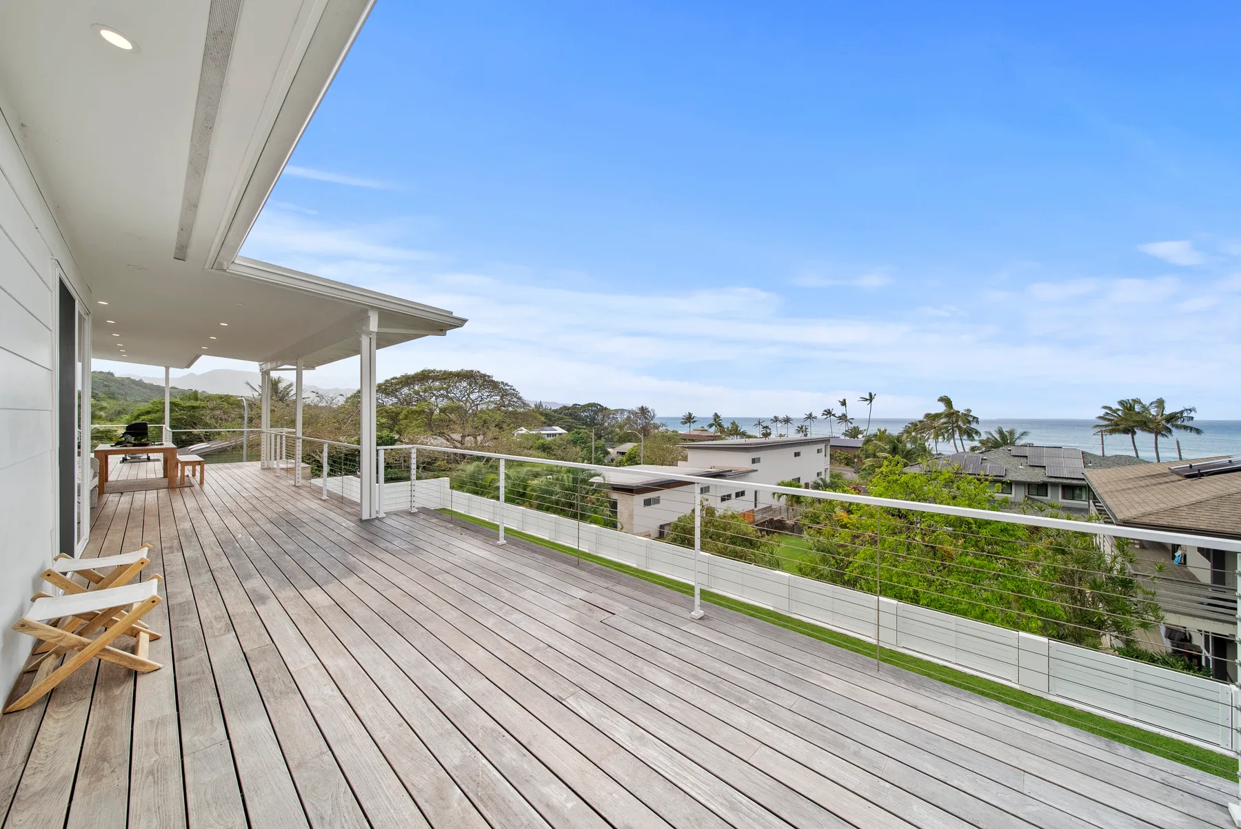 A spacious outdoor deck overlooks nearby homes, greenery, and the ocean.