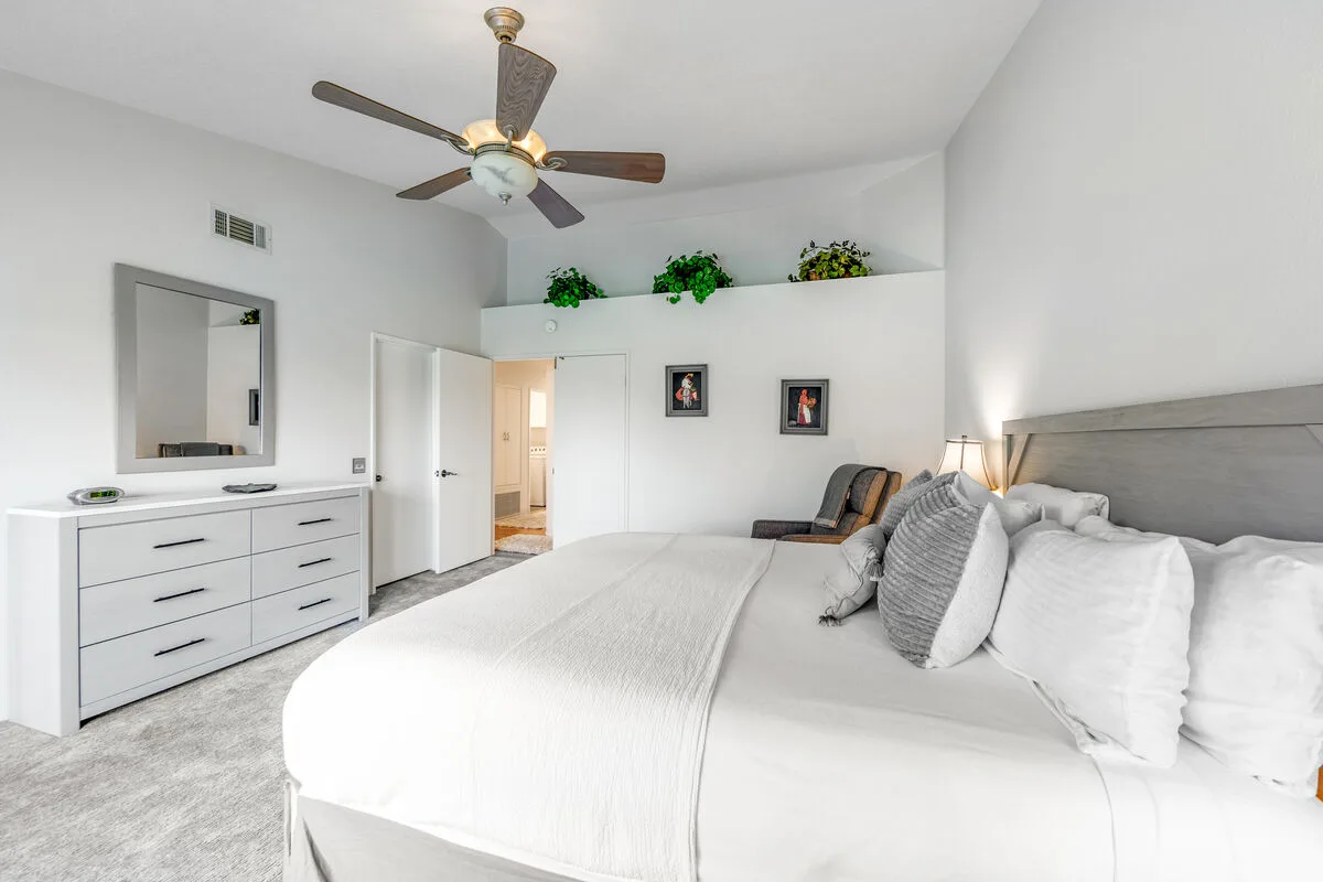 Un dormitorio luminoso con una cama grande, una cómoda y un ventilador de techo.