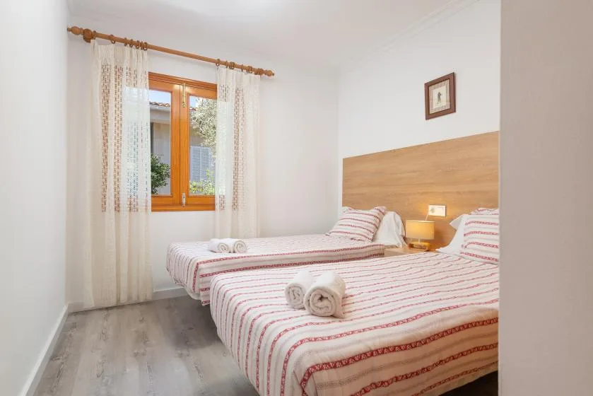 A bright bedroom with two beds and a window with curtains.