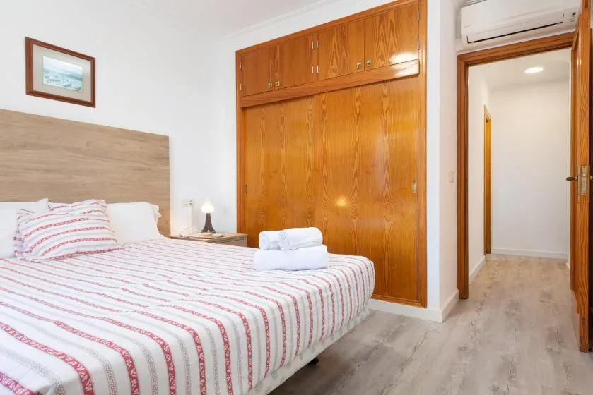 A bedroom with a striped bed and wooden wardrobe beside an open doorway.