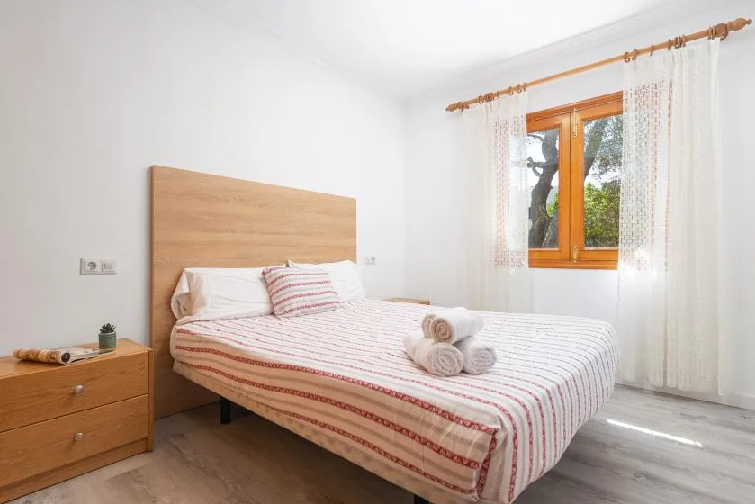 A bright bedroom with a bed dressed in white and red-striped bedding.